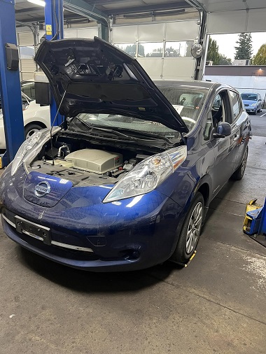 Blue Nissan Leaf electric car in service bay with hood open showing battery